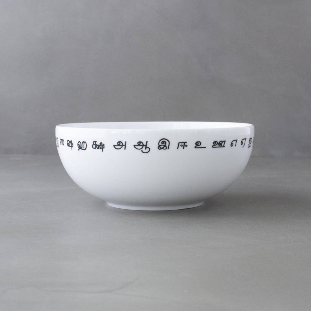 A white ceramic bowl with black Tamil script printed around the rim, set against a neutral gray background.